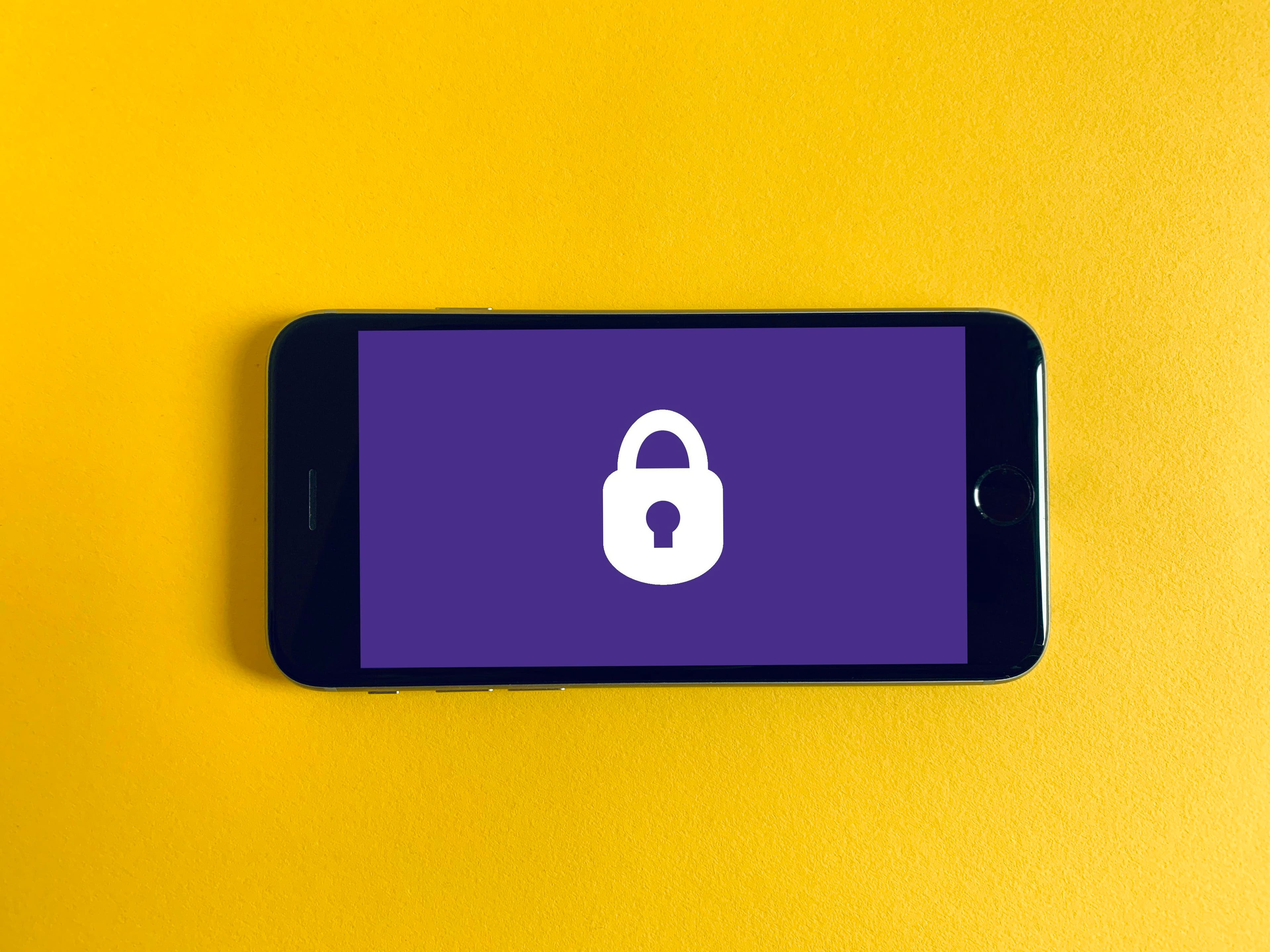 Смартфон с иконкой замка на экране на жёлтом фоне — телефон как хранилище ключей доступа passkeys