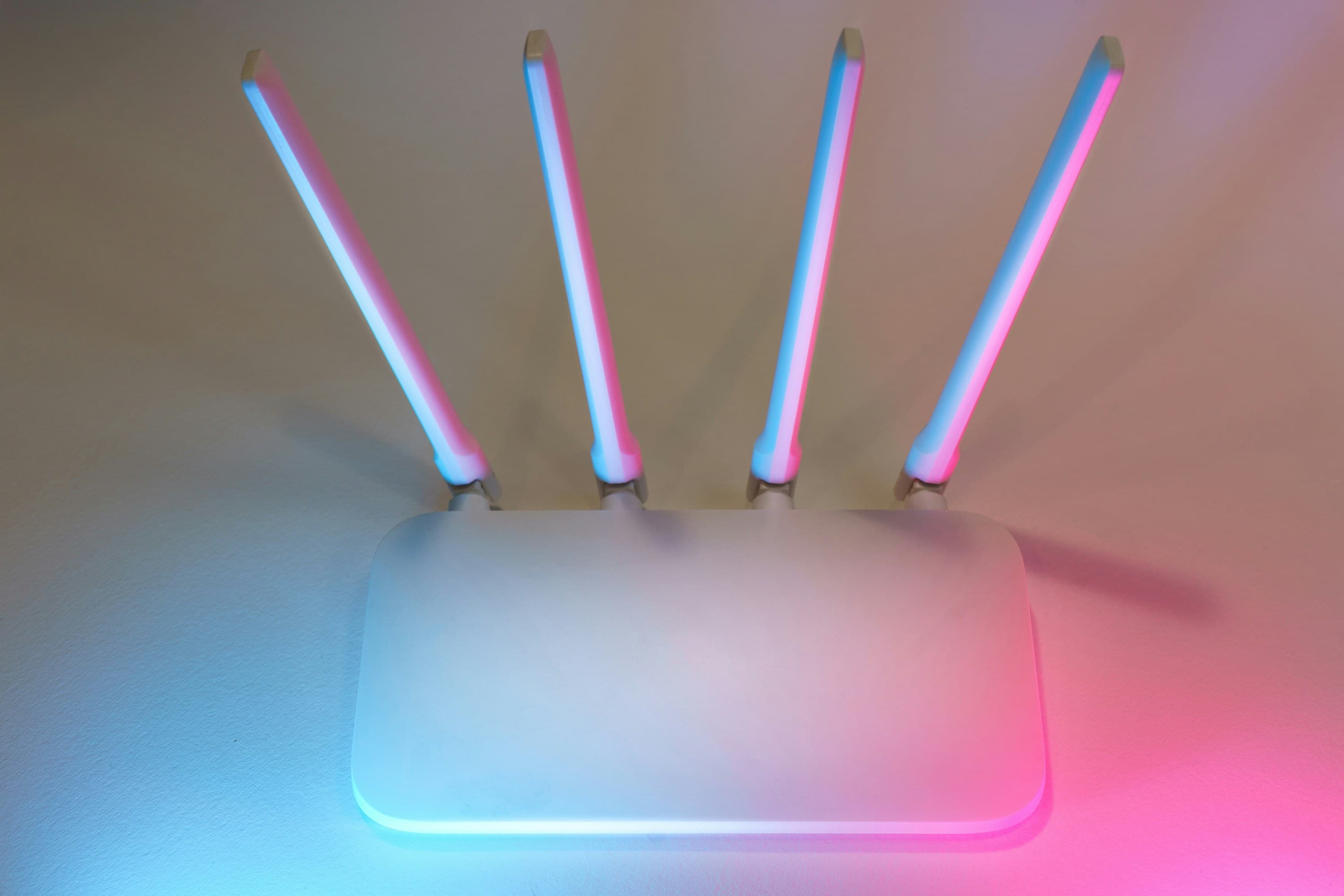 Белый Wi-Fi-роутер с четырьмя антеннами в розово-голубой подсветке — домашний роутер, который важно правильно настроить для безопасности сети